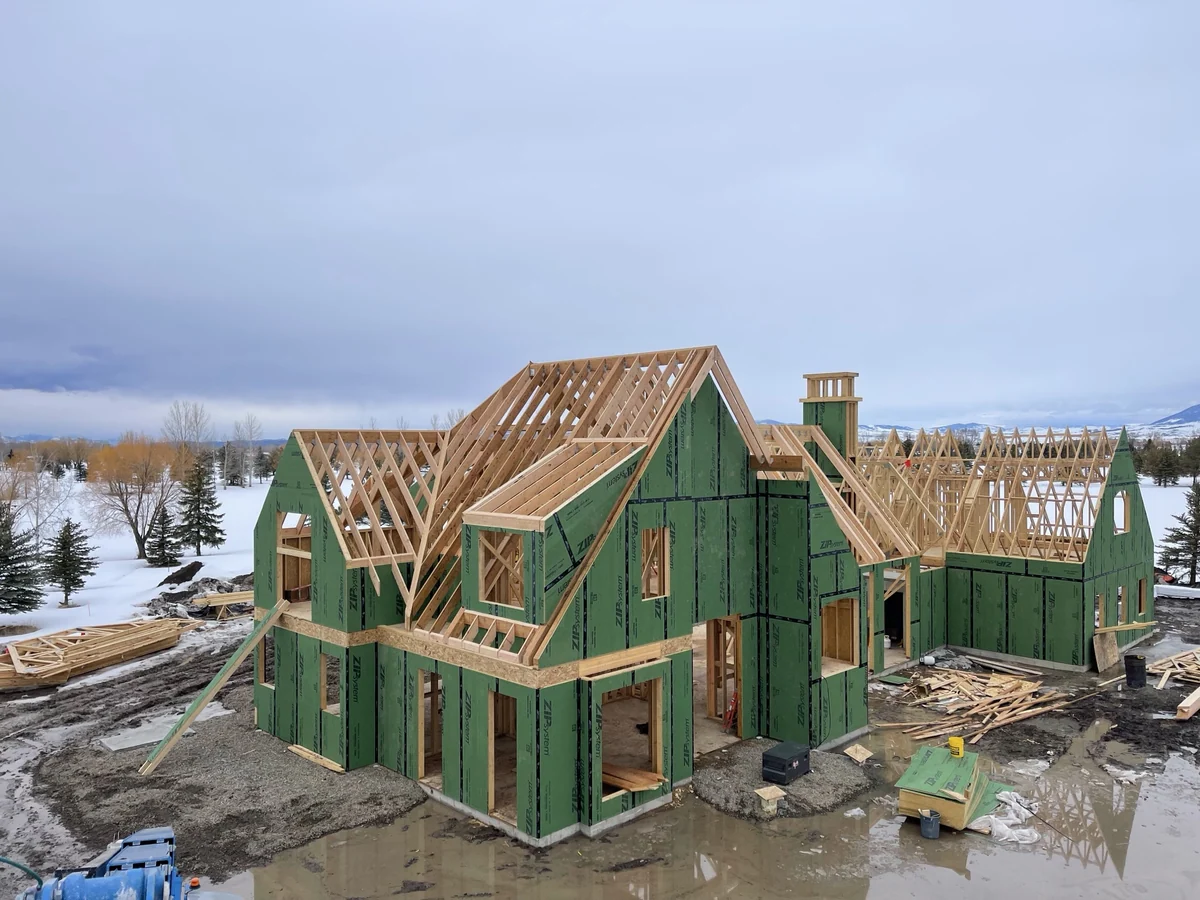 A large custom home framed and sheathed with steep gables, dormers and a chimney chase, snow on the ground and mountains behind