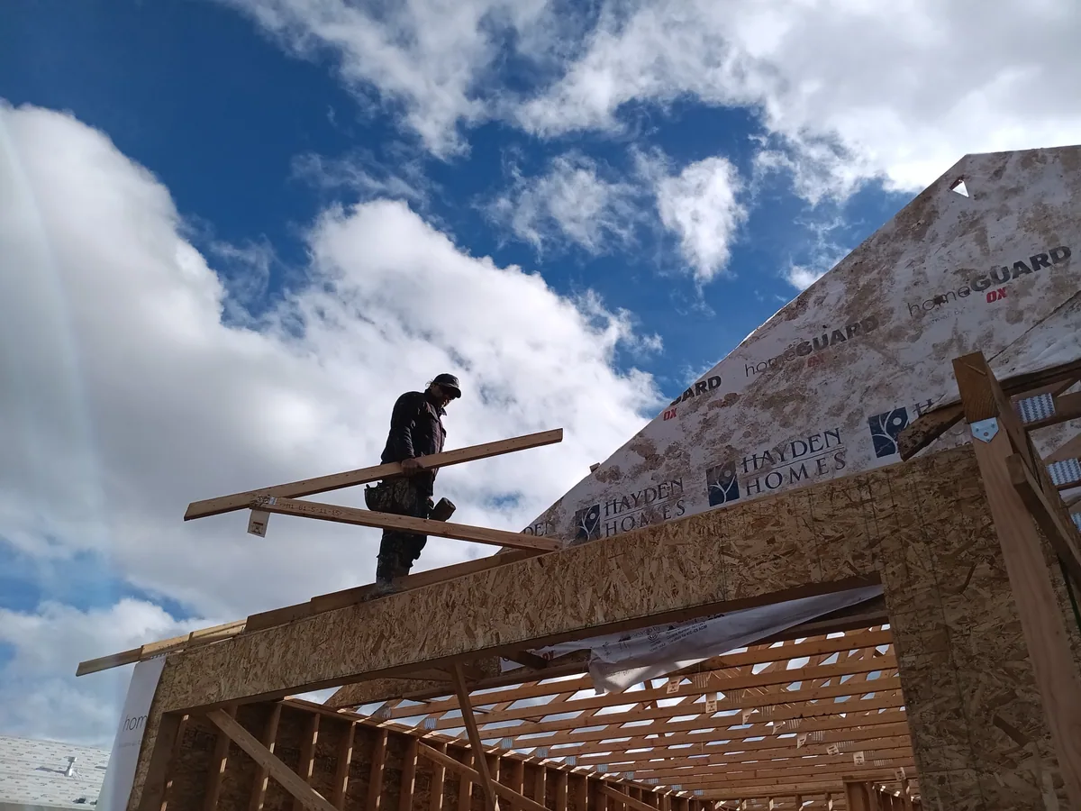 One of our carpenters carrying a board across a framed wall against an open Montana sky