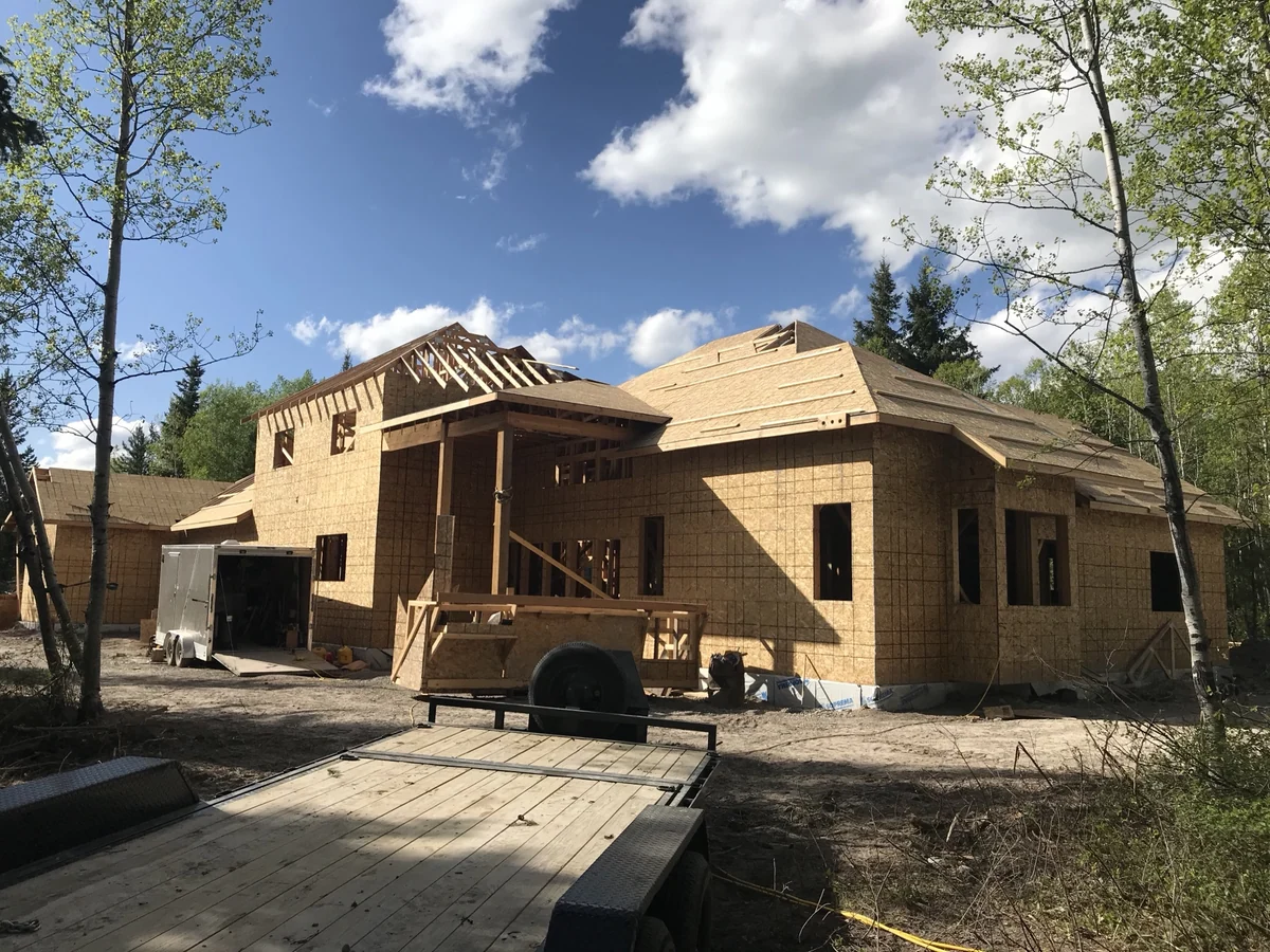 A new home framed with roof sheathing going on, blue sky and timber behind